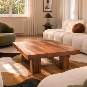 Table basse CENT-SIX en bois naturel dans un salon lumineux avec canapé blanc et fauteuil vert.