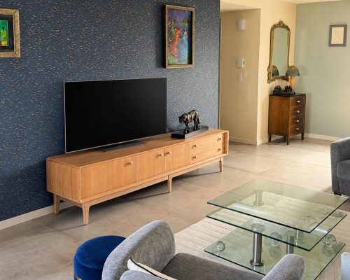 Enfilade vintage en teck naturel dans un salon moderne avec décoration élégante et mur bleu foncé.